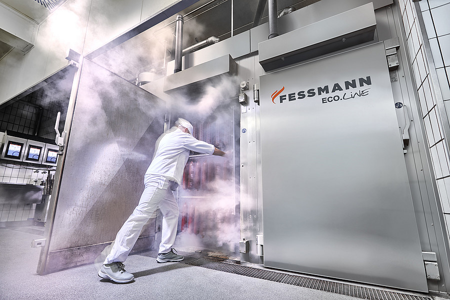 employee pushing rack of smoked meats into a Fessmann smokehouse