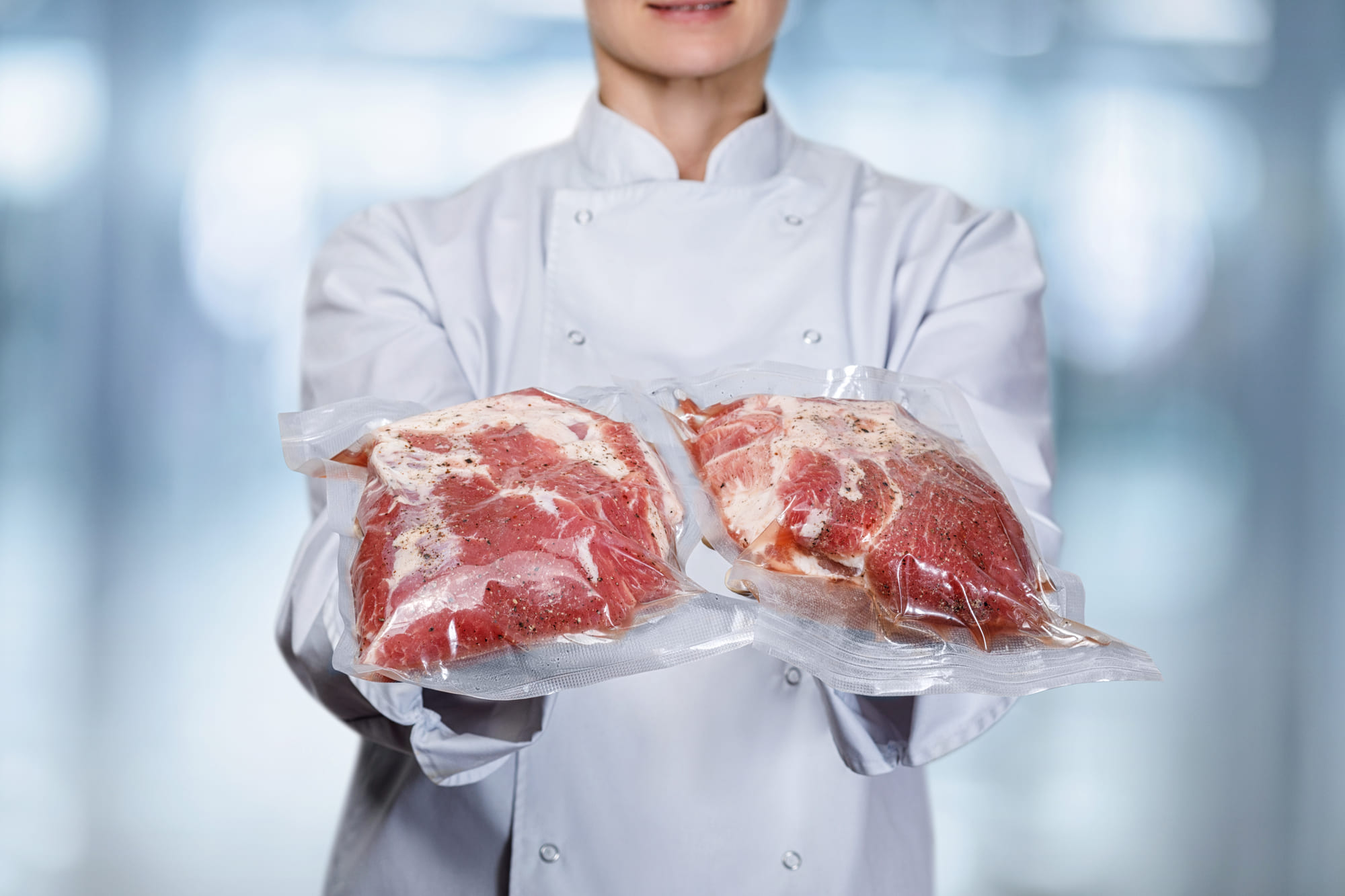 a chef holding up 2 wrapped up pieces of meat intended for a sous vide cooker